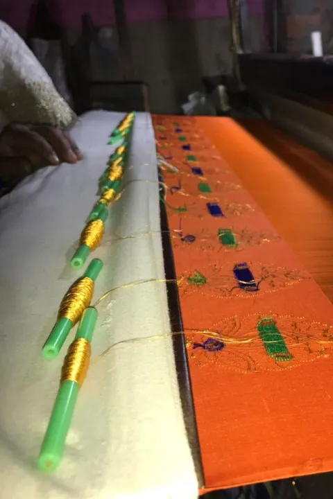 Bobbins of gold zari and coloured thread resting on a saree being woven